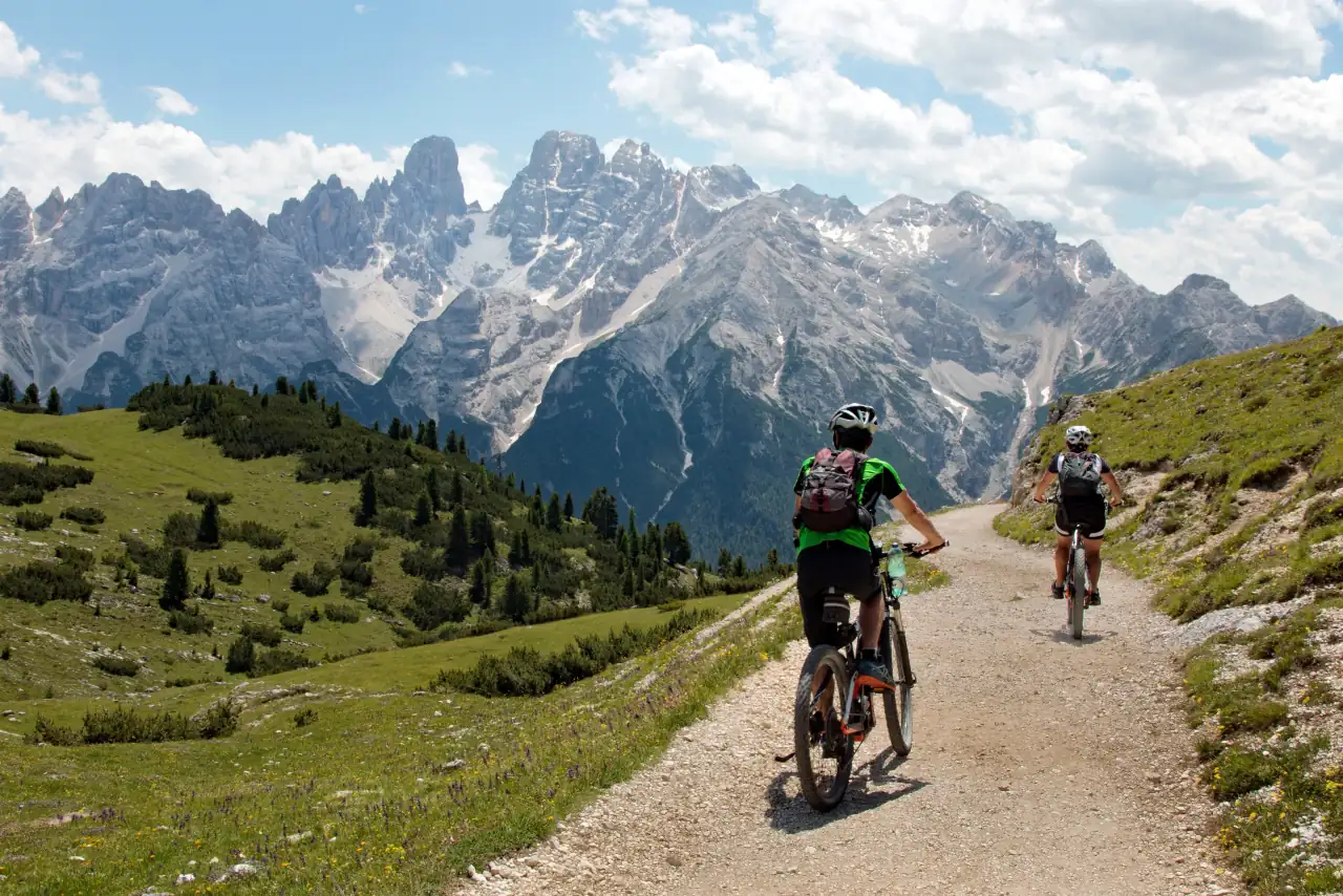 Due ciclisti in mountain bike su una strada bianca davanti alle Dolomiti d'estate